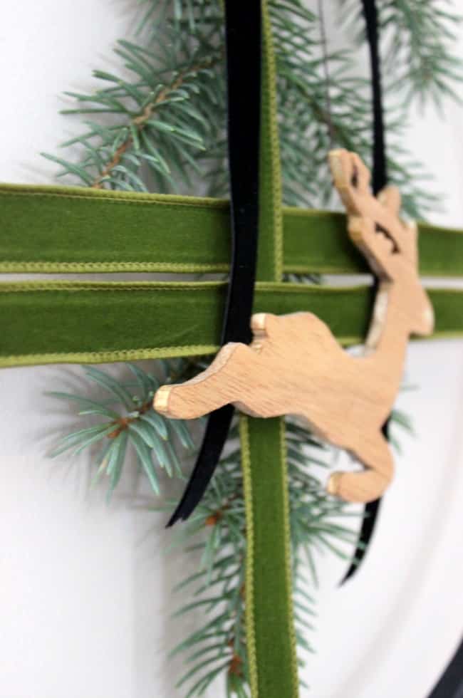 Modern Christmas wreath with wooden deer and green velvet ribbon.