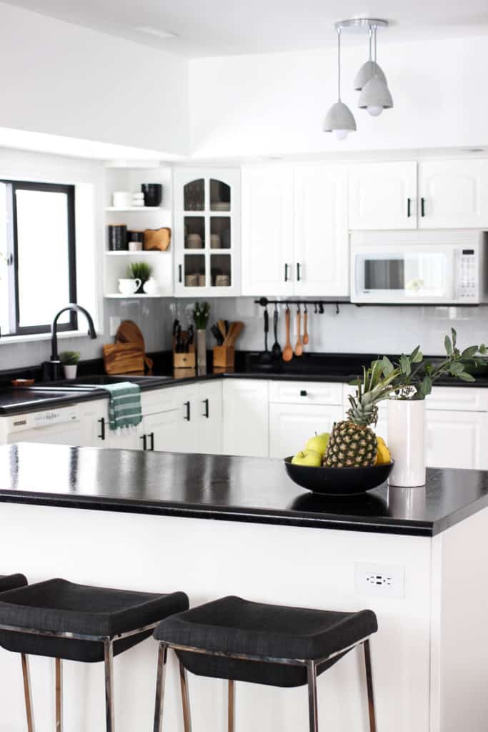 Wow! This stunning modern kitchen was transformed in just one weekend! Love the design ideas in this stunning black and white kitchen! The kitchen features white cabinets, black countertops, black hardware, matte black faucet, black sink, and wood accents. The use of countertop paint and peel and stick tile was brilliant!