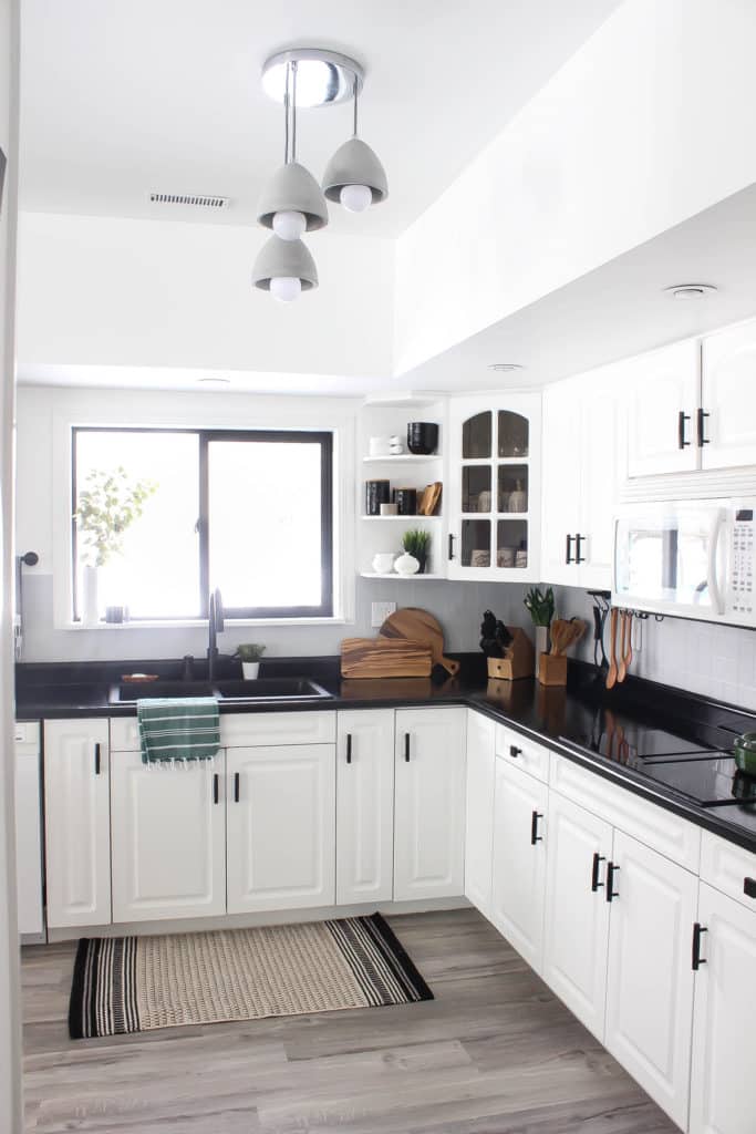 Wow! This stunning modern kitchen was transformed in just one weekend! Love the design ideas in this stunning black and white kitchen! The kitchen features white cabinets, black countertops, black hardware, matte black faucet, black sink, and wood accents. The use of countertop paint and peel and stick tile was brilliant!