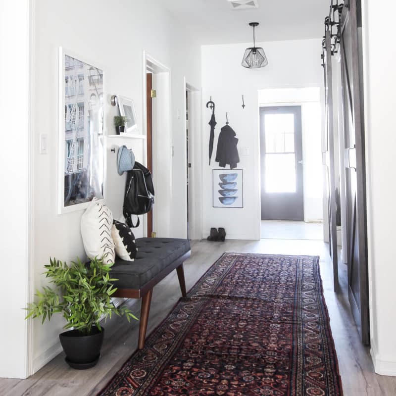 Beautiful hallway decor ideas! Love the eclectic mix of materials and styles in this space. Beautiful light flooring, gorgeous overlapping barn doors, modern artwork, and a vintage hallway runner complete the space. Perfect ideas to fill up a wide hallway!