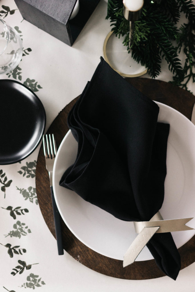 A stunning holiday tablescape and DIY table runner! This beautiful modern table setting was put together with a few affordable painted pieces creating a beautiful dark a moody Christmas table with greens, blacks, and whites. The eucalyptus stamped table runner is gorgeous! #tablescape #Christmas #darkandmoody #Holiday #blackandwhite #tablesetting