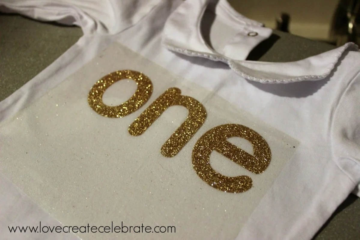 Glitter one placed on onesie for heat transfer