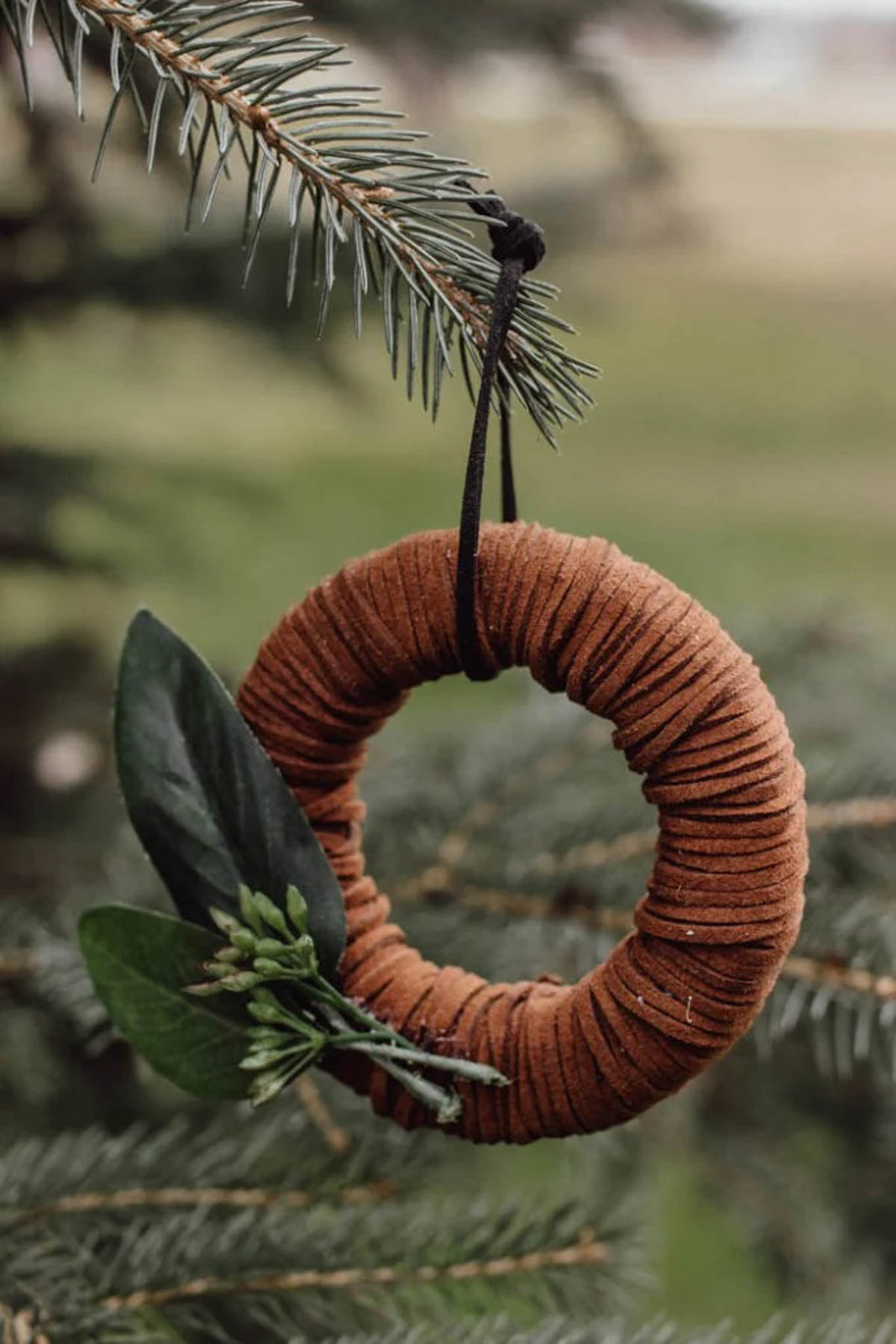 Mini wreath ornament with leather hanging from a tree.