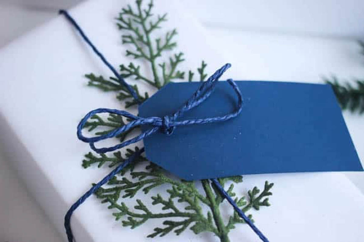 DIY gift wrap with greenery and a blue tag.