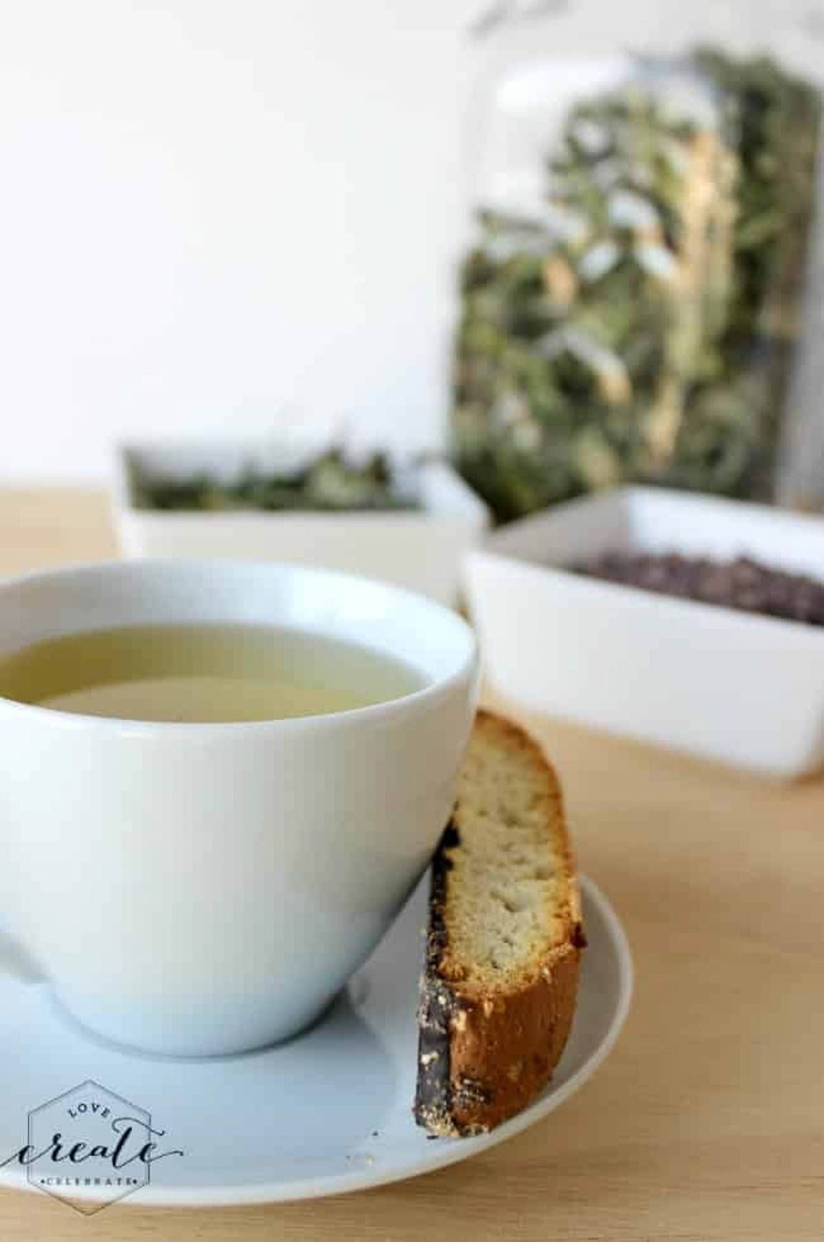 Cup of tea with a biscotti and bowls of herbs.