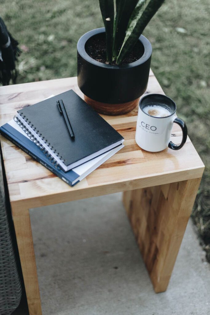 Close up image of table top with plant, coffee mug and notebooks and pen