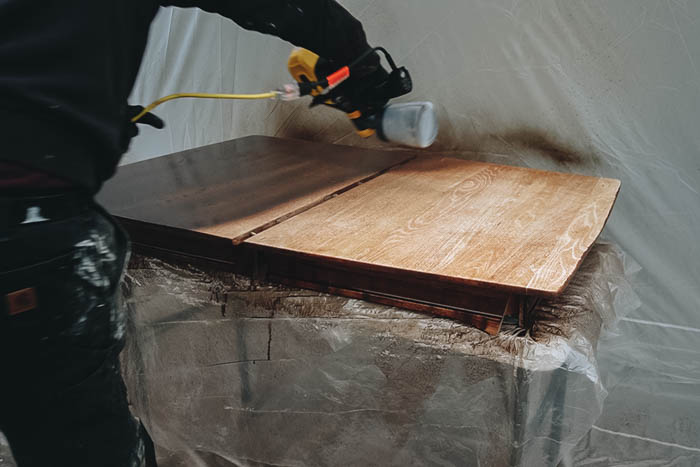 applying stain to table top with sprayer 